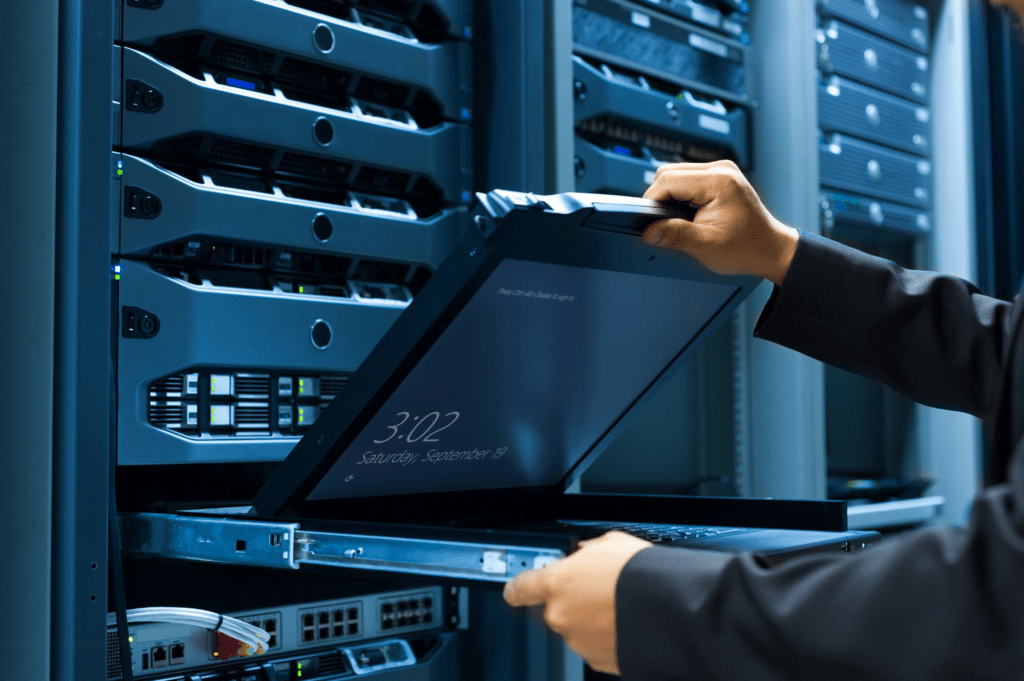 A person uses a laptop integrated into a server rack in a dimly lit data center. The screen shows 3:02 on Saturday, September 21. Surrounded by rows of servers, this setup exemplifies efficient managed server solutions.