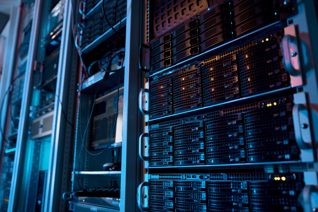 A close-up view of a server room with several racks of servers showcases the complexity of cybersecurity consulting. The equipment is illuminated by blue and purple lights, highlighting the intricate organization of cables and server units crucial for securing sensitive information.