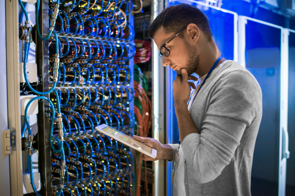 a man with a tablet in front of a network rack