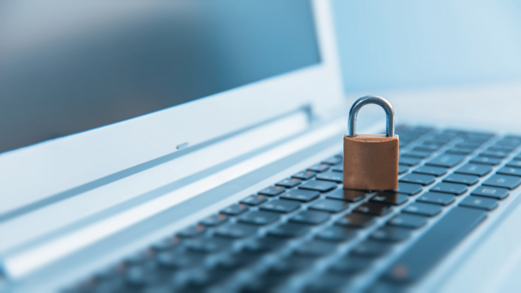 A small padlock sits on the keyboard of an open laptop, symbolizing Endpoint Security. The image is in soft focus with a light blue tint, emphasizing the concept of online safety and advanced endpoint security solutions.