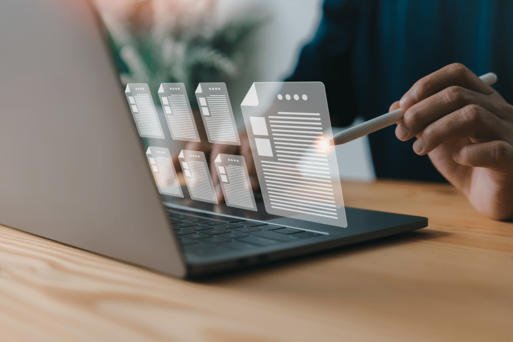 A person uses a stylus to interact with digital documents displayed as holographic images over a laptop on a wooden desk. This setup, enhanced by managed IT services for law firms, suggests an innovative approach to document management in the legal sector.