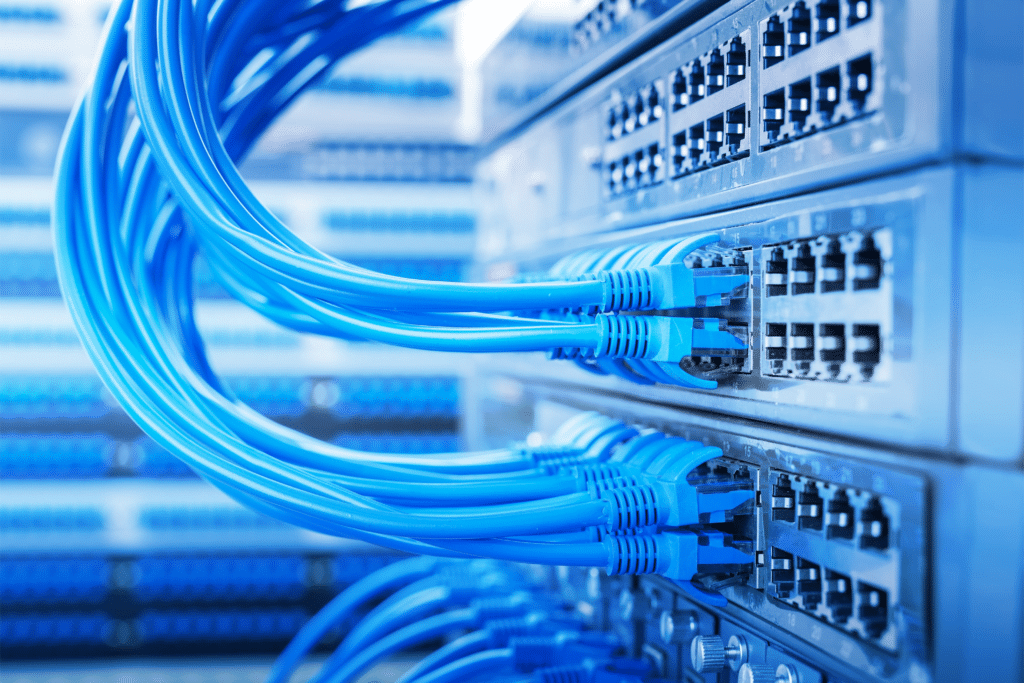 Close-up of blue network cables plugged into a row of server racks. These cables, crucial to the network-infrastructure, are connected to multiple ports, emphasizing a data center or server room environment with other servers blurred in the background.