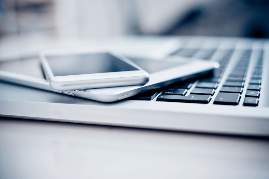 A close-up of two smartphones stacked on a laptop keyboard highlights the seamless integration of mobile device management. The devices are sleek and modern, with a blurred background, emphasizing technology's role in enhancing security and productivity through connectivity.