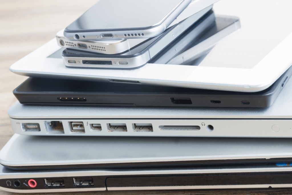 A stack of various electronic devices, including smartphones, a tablet, and multiple laptops, placed on a light wood surface. This assortment highlights Mobile Device Management: Enhancing Security and Productivity by showcasing different ports and connectors that adapt to user needs.