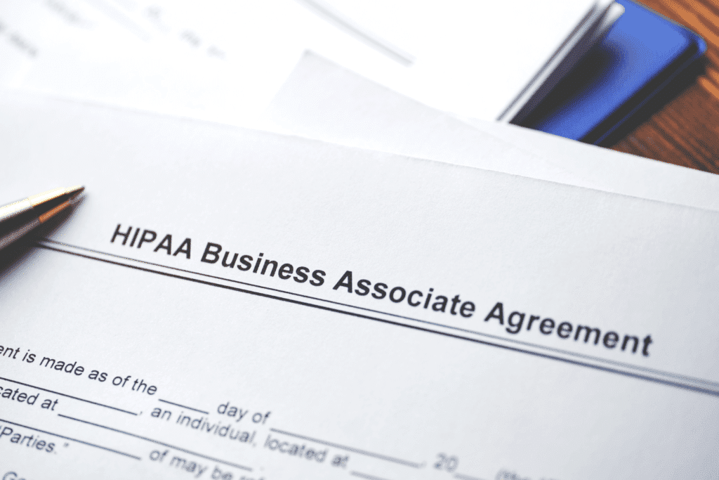 A close-up of a document titled HIPAA Business Associate Agreement highlights the importance of HIPAA-compliant IT services. A pen rests on the paper in the top left corner, signaling readiness for signing and ensuring data security and compliance. Other pages are partially visible underneath.