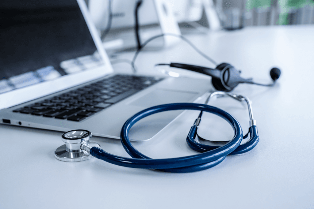 A stethoscope and headset rest on an open laptop on a white desk, symbolizing telemedicine or healthcare technology. The softly blurred background highlights the focus on digital medical tools, emphasizing the importance of HIPAA-compliant IT services in ensuring data security and compliance.