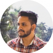 A bearded person with short hair wearing a red plaid shirt stands outdoors, gazing to the side. The background features blurry green foliage and a hint of blue sky—an ideal visual for an engaging homepage template.