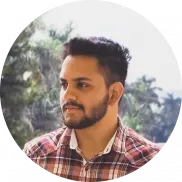 A man with short dark hair and a beard, wearing a red plaid shirt, looks to the side. Palm trees and a bright sky are visible in the background, capturing a relaxed moment away from his role providing managed IT services.